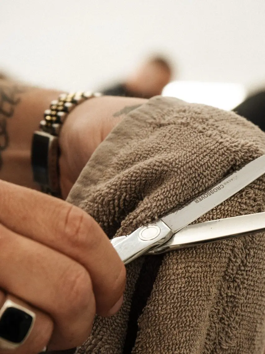 A barber wiping his scissors on a hot towel between clients